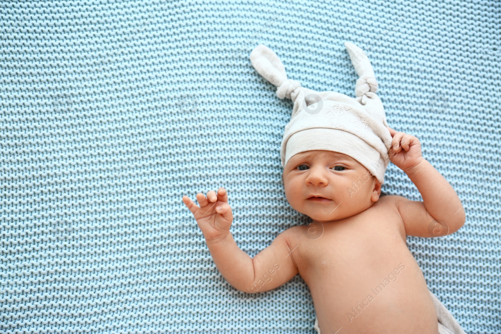 Photo of Cute little baby in hat lying on light blue plaid, top view. Space for text
