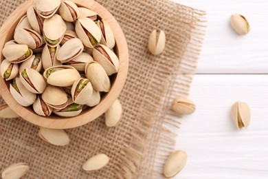 Photo of Tasty pistachios in bowl on white wooden table, top view. Space for text