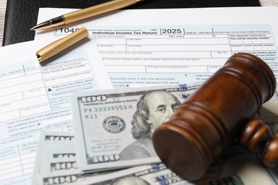 Photo of Tax return forms, dollar banknotes, gavel and pen on table, closeup