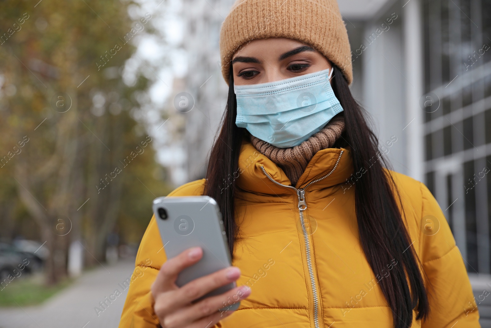 Photo of Young woman in medical face mask with smartphone walking outdoors. Personal protection during COVID-19 pandemic