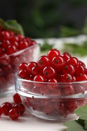 Photo of Many ripe red currants and leaves on white table, closeup