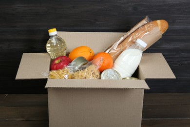 Photo of Cardboard box with donation food on wooden table, closeup