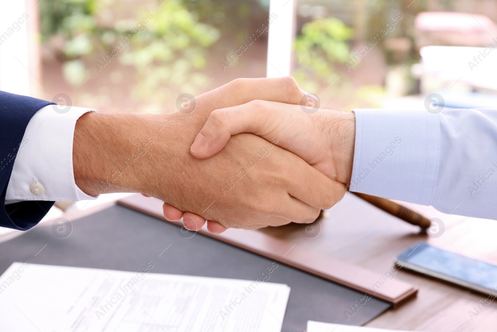 Photo of Lawyer handshaking with client over table in office, closeup