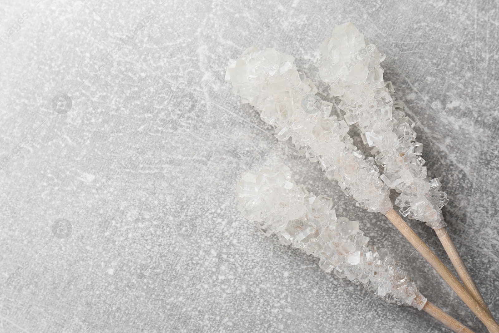 Photo of Wooden sticks with sugar crystals on light grey table, flat lay and space for text. Tasty rock candies