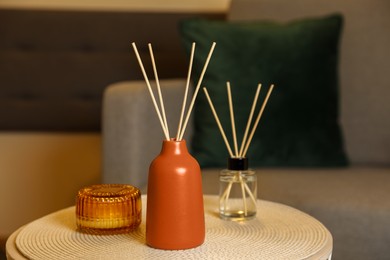 Aromatic reed air fresheners and scented candle on table indoors