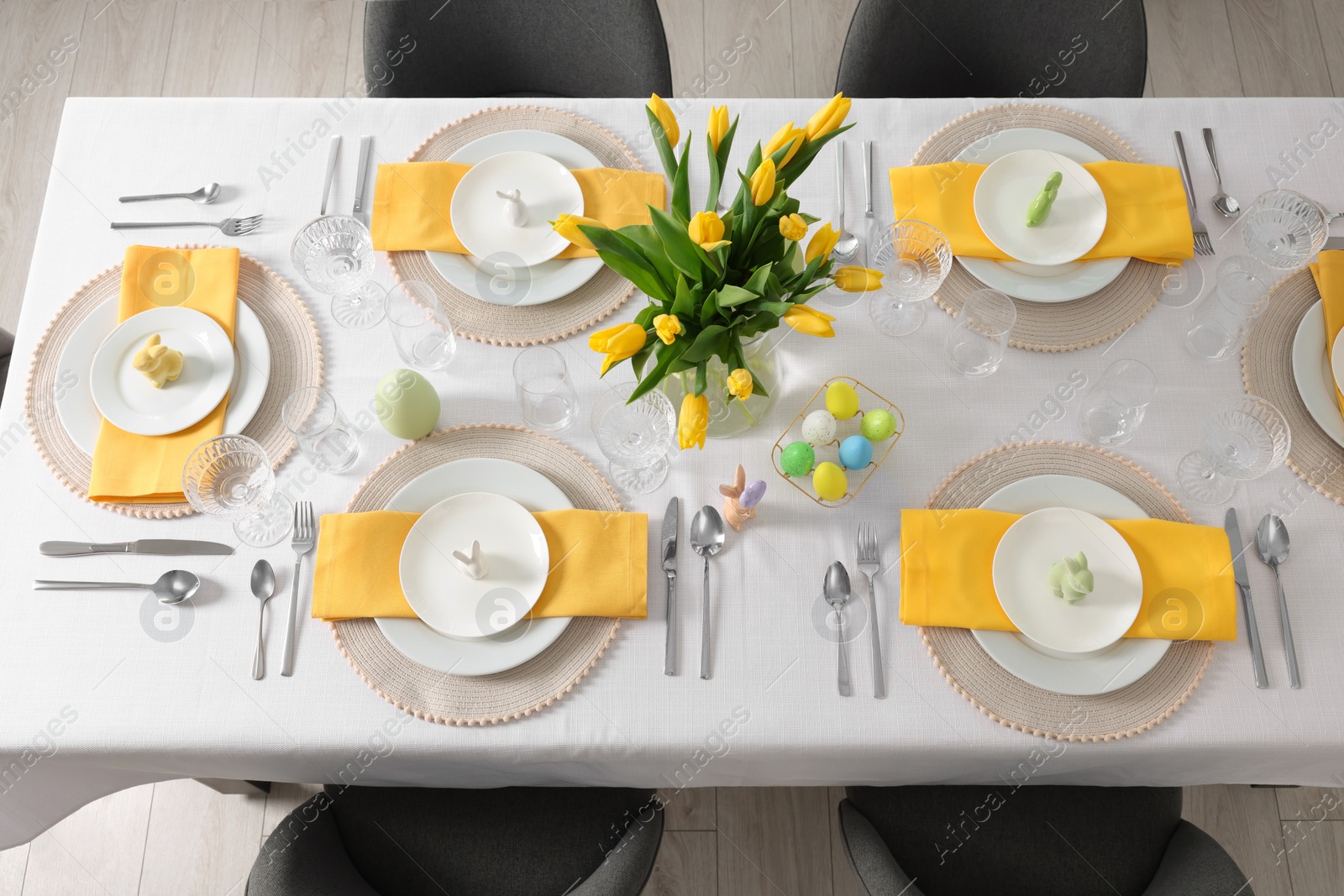 Photo of Festive table setting with glasses, painted eggs and vase of tulips, view from above. Easter celebration