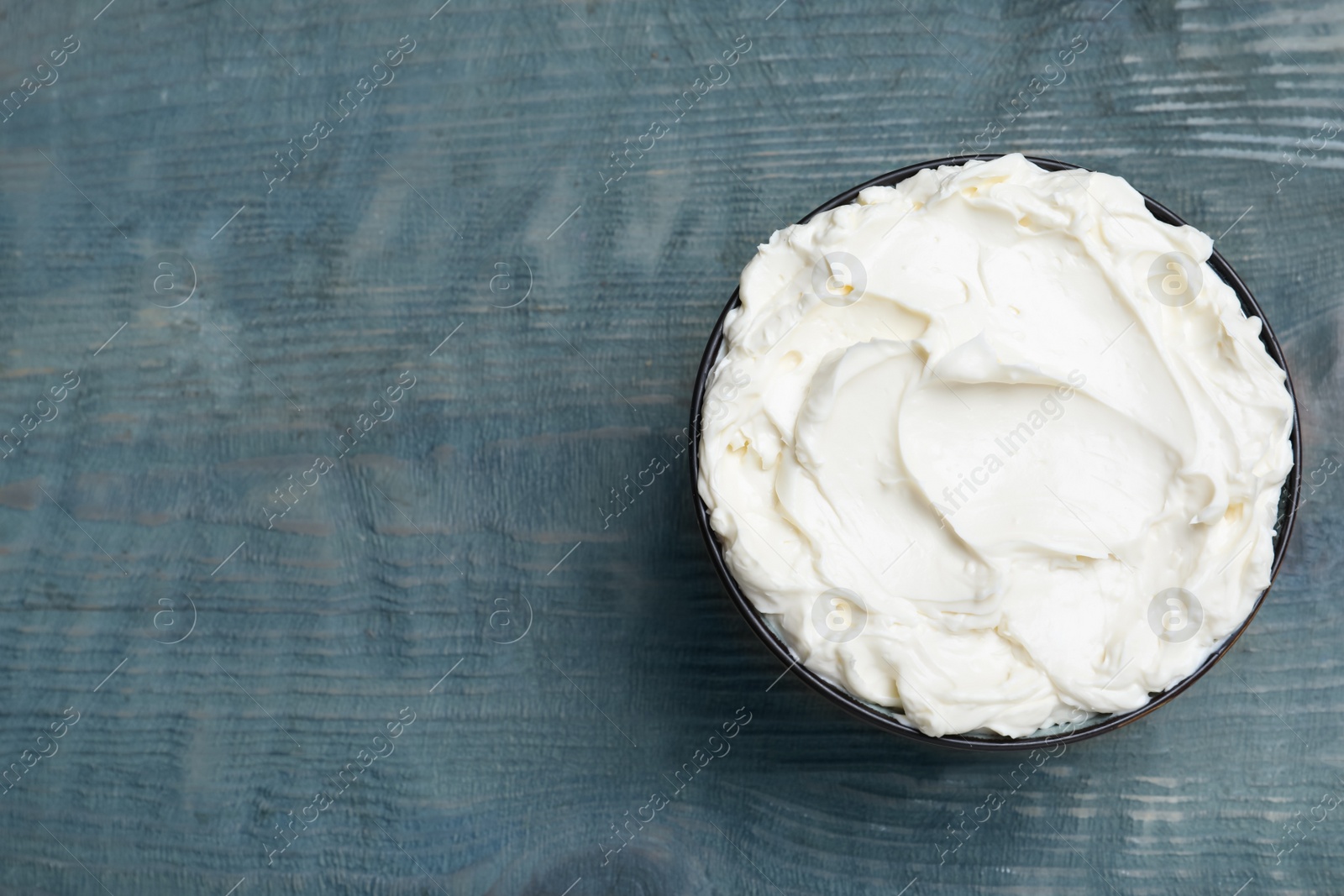 Photo of Tasty cream cheese on light blue wooden table, top view. Space for text
