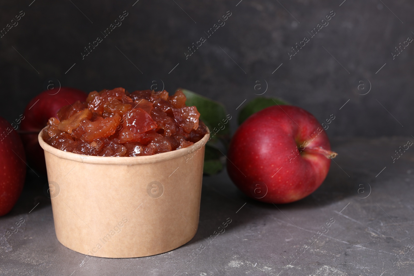 Photo of Delicious apple jam and fresh fruits on grey table. Space for text