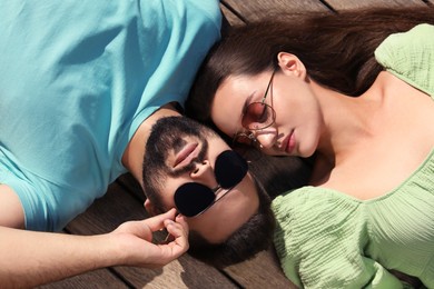 Photo of Beautiful woman and handsome man in sunglasses on wooden deck outdoors, above view