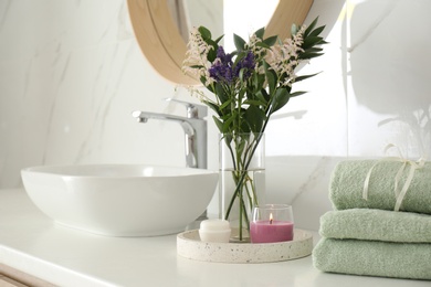 Photo of Beautiful flowers, towels and candle on countertop in bathroom. Interior decor