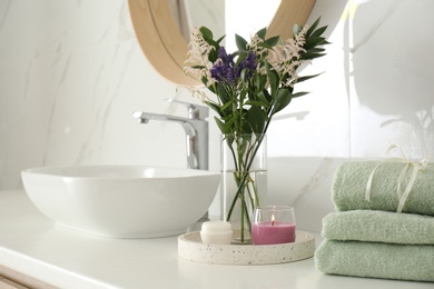 Beautiful flowers, towels and candle on countertop in bathroom. Interior decor