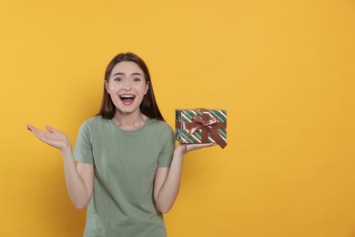 Portrait of emotional young woman with gift box on yellow background. Space for text