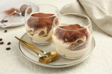 Photo of Delicious tiramisu in glasses, spoons and coffee beans on white table