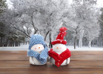 Image of Cute decorative snowmen on wooden table in snowy forest