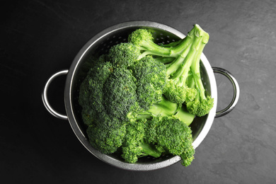 Photo of Fresh green broccoli in colander on black table, top view