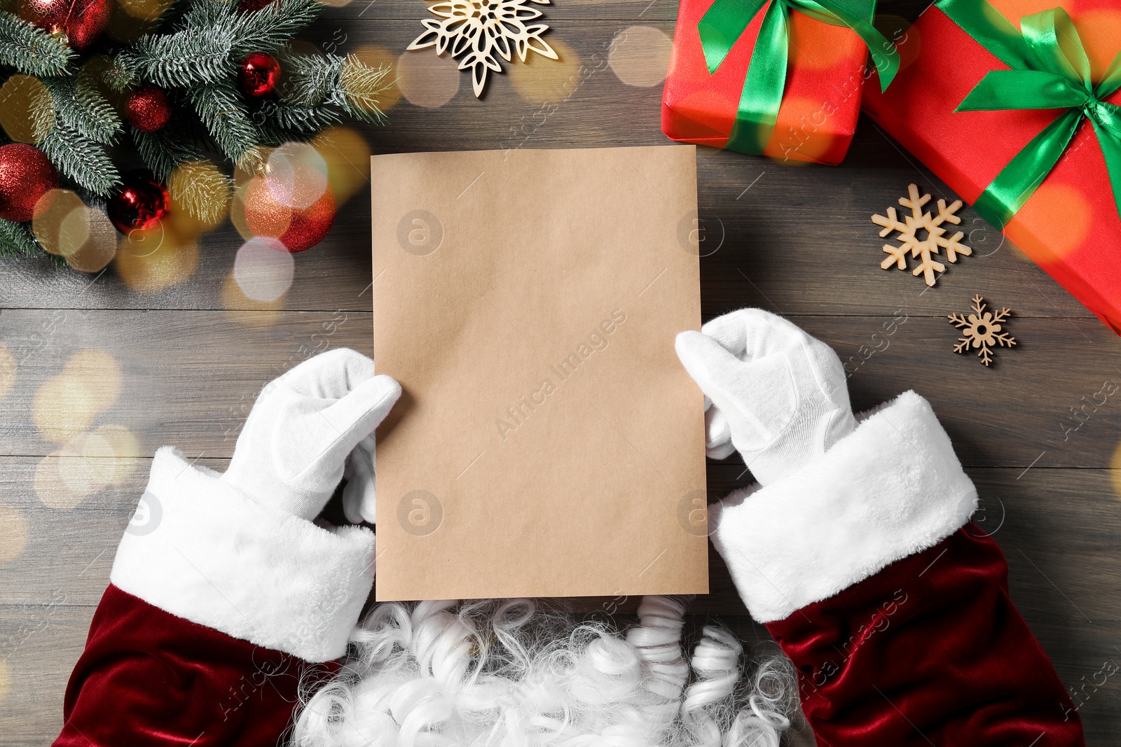 Photo of Santa Claus with letter, gift boxes and Christmas decor at wooden table, top view. Space for text