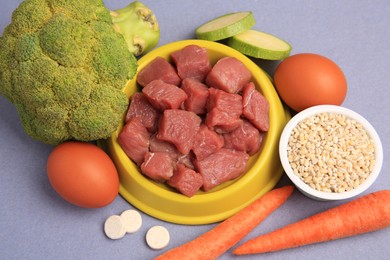 Raw meat in bowl, vitamins and products for pet on color background, flat lay
