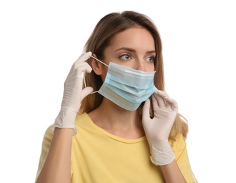 Woman in medical gloves putting on protective face mask against white background
