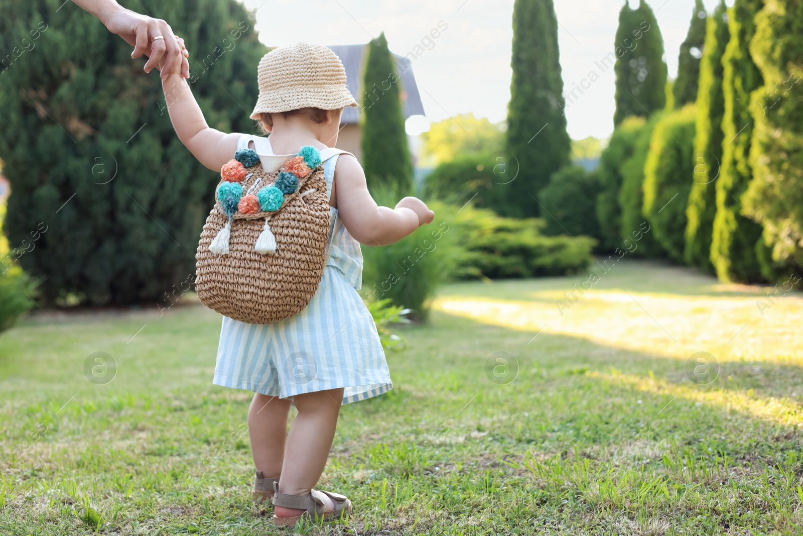 Photo of Cute little girl in stylish clothes holding mother's hand outdoors on sunny day, back view. Space for text