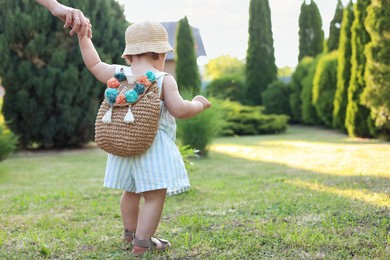 Photo of Cute little girl in stylish clothes holding mother's hand outdoors on sunny day, back view. Space for text