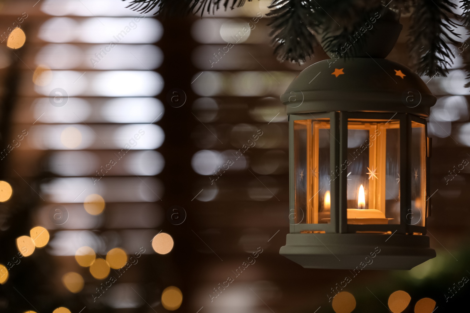 Photo of Beautiful Christmas lantern with burning candle hanging on fir tree branch in room. Space for text