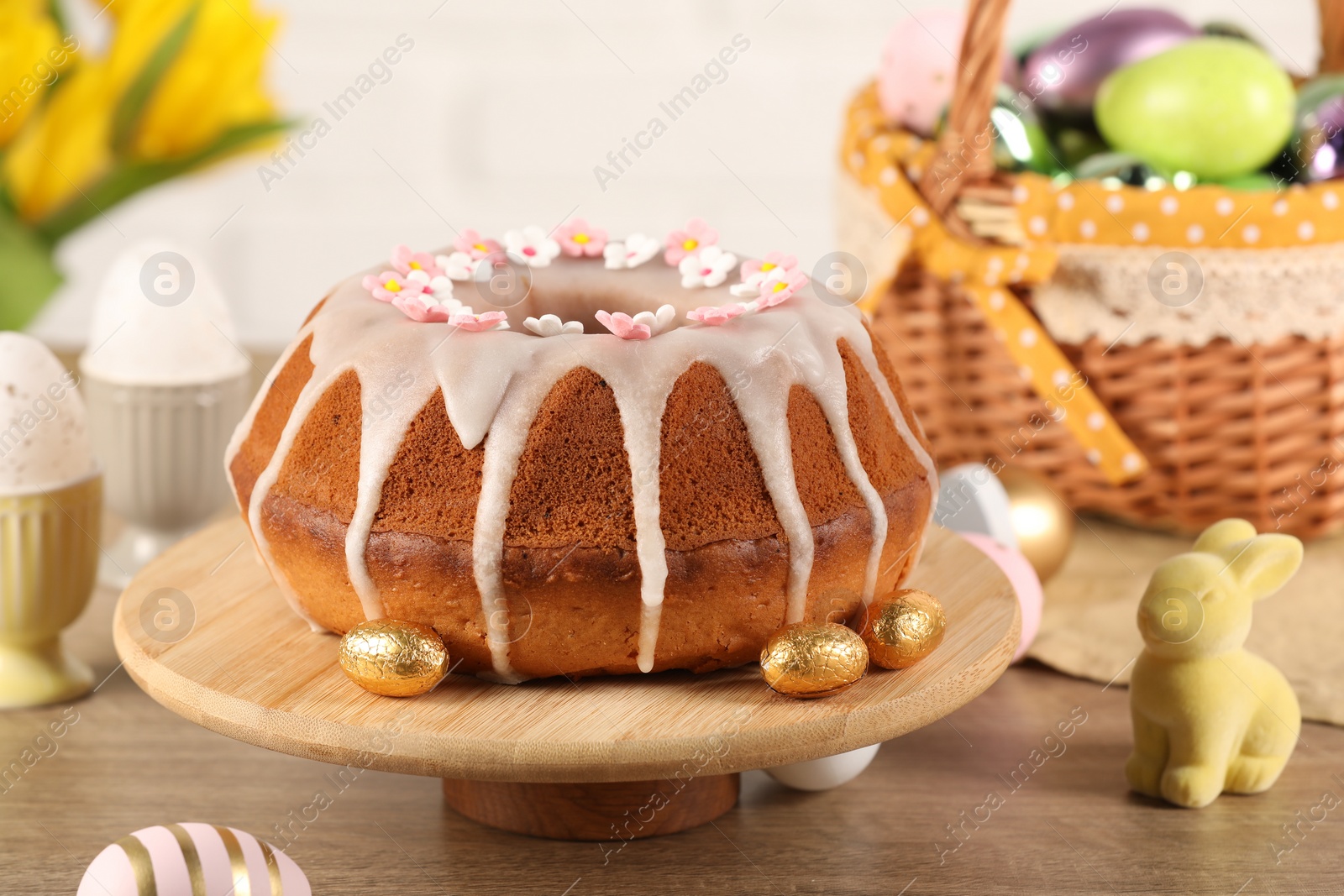 Photo of Delicious Easter cake decorated with sprinkles near eggs and rabbit figure on wooden table