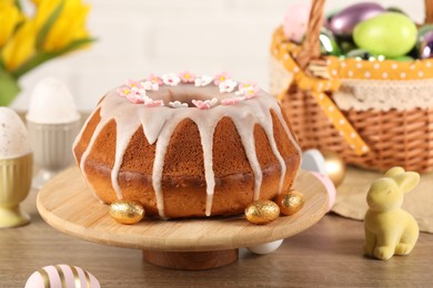 Photo of Delicious Easter cake decorated with sprinkles near eggs and rabbit figure on wooden table