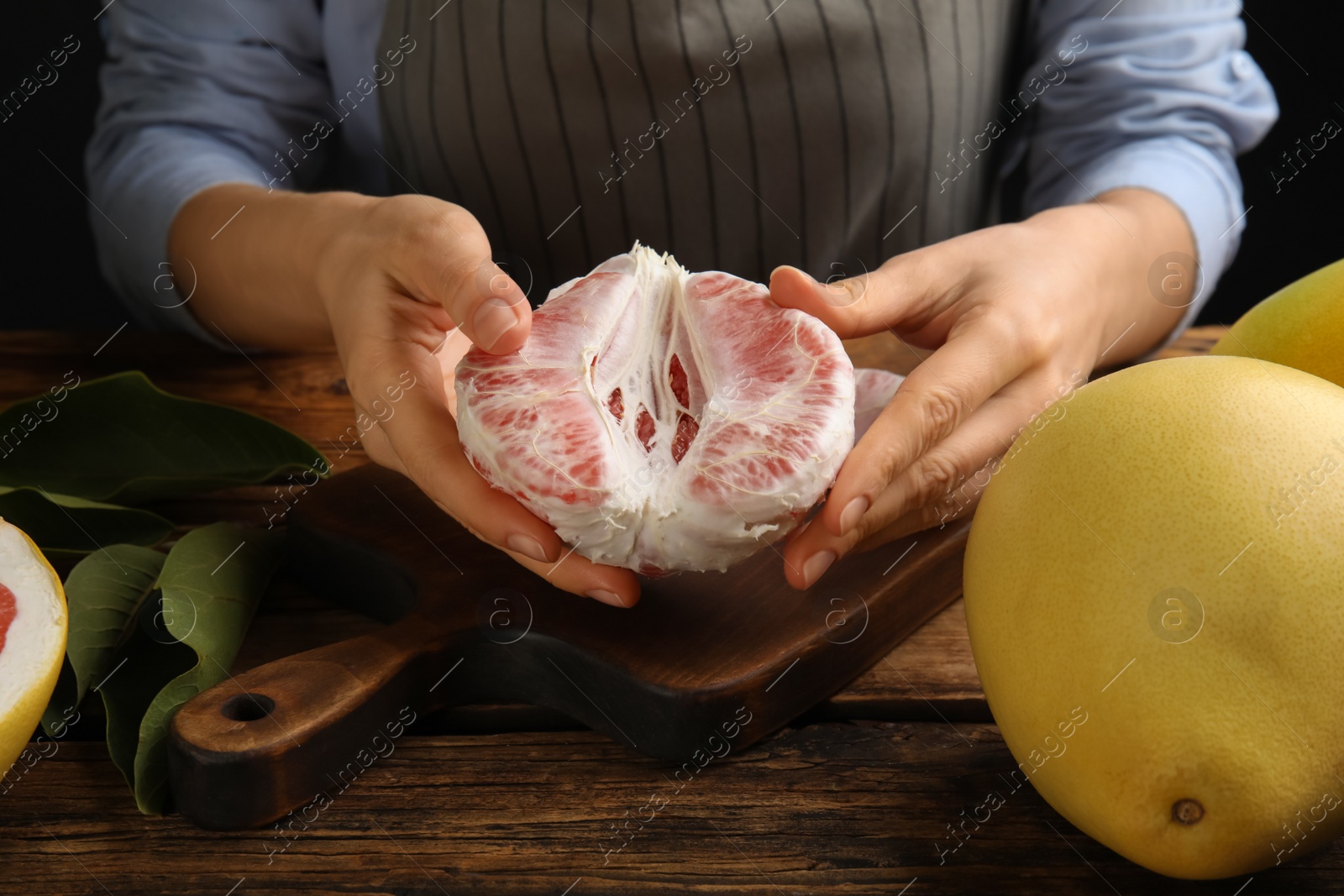 Photo of Woman with tasty red pomelo at wooden table, closeup