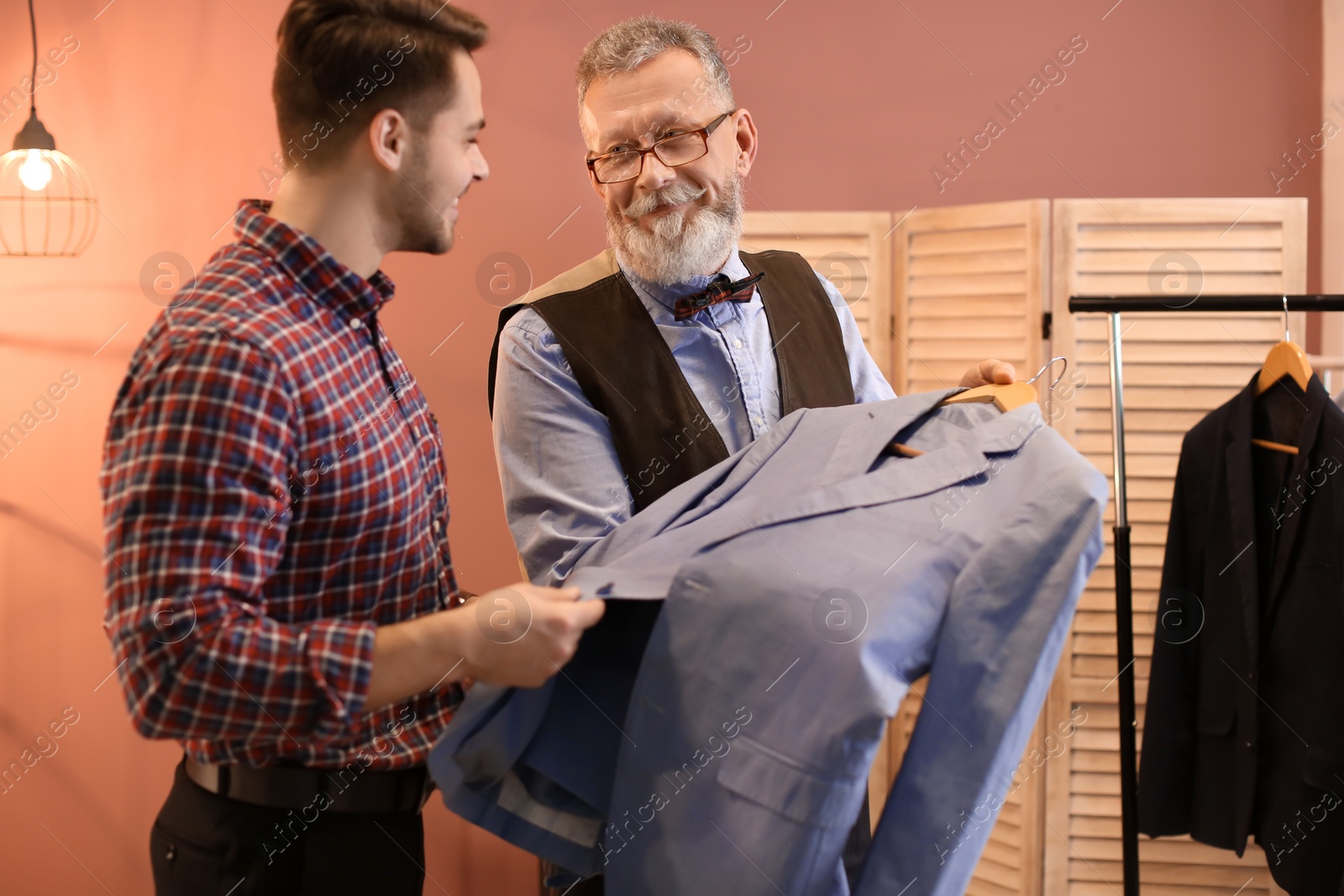 Photo of Mature tailor showing jacket to client in atelier