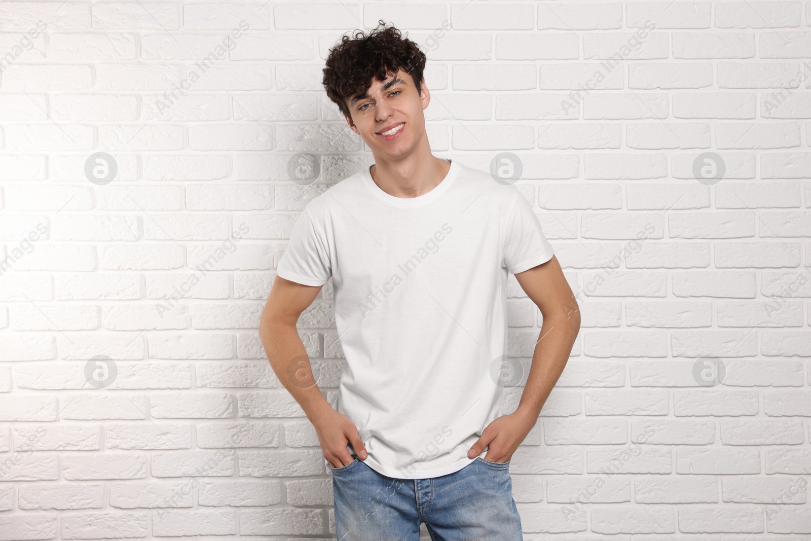 Photo of Man wearing stylish t-shirt near white brick wall. Mockup for design