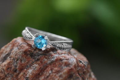 Photo of Beautiful ring with light blue gemstone on stone, closeup. Luxury jewelry