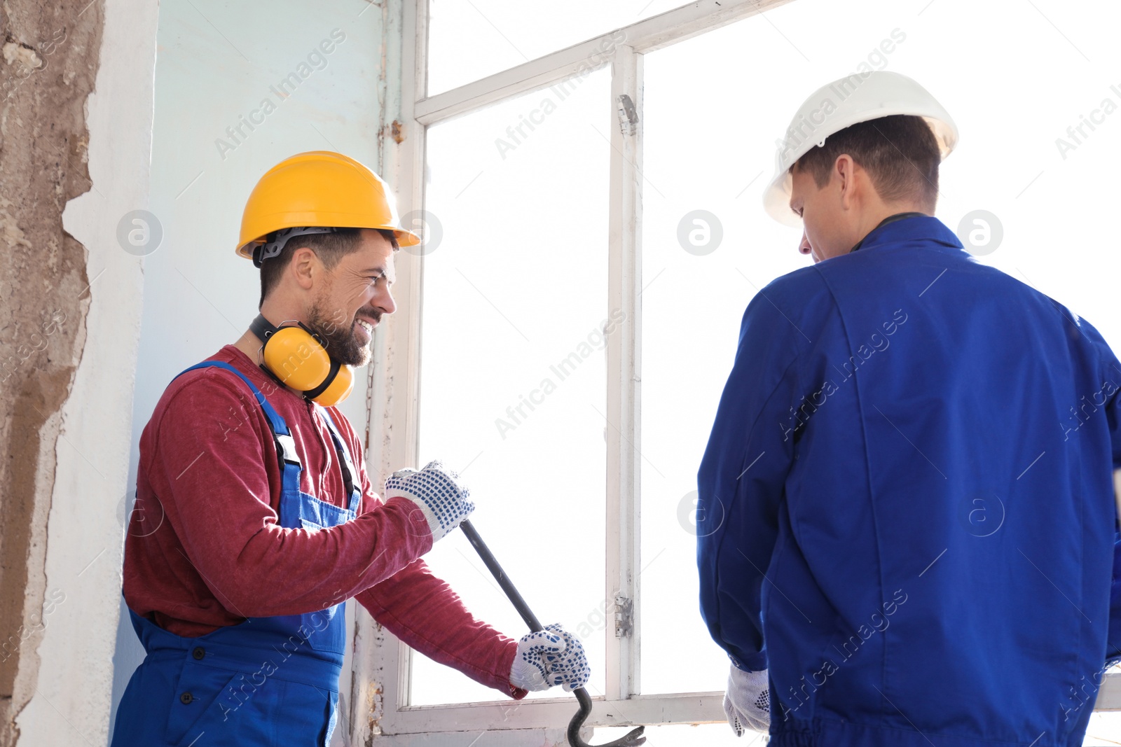 Photo of Workers dismantling old window with crowbar indoors