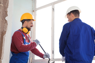 Workers dismantling old window with crowbar indoors