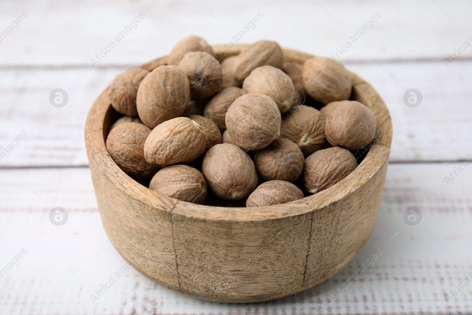 Photo of Whole nutmegs in bowl on light wooden table, closeup