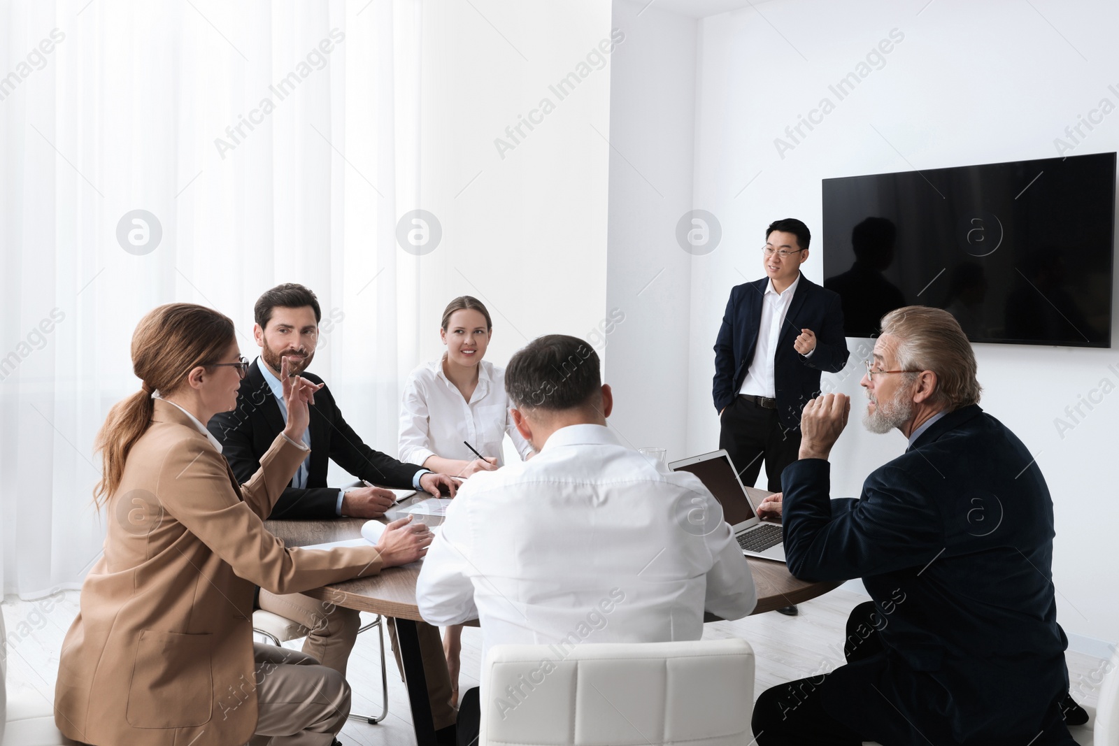 Photo of Business conference. Group of people listening to speaker report near tv screen in meeting room