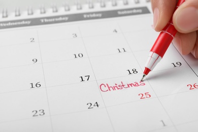 Photo of Woman writing word Christmas on calendar, closeup. Holiday countdown