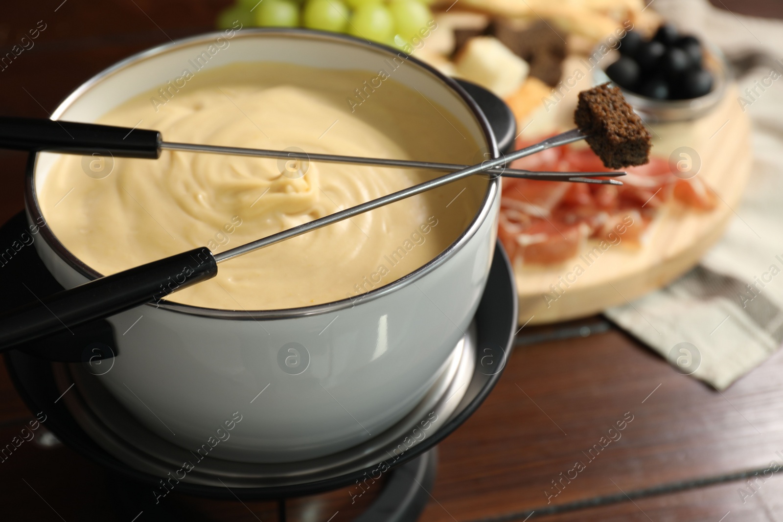 Photo of Fondue with tasty melted cheese, forks and piece of bread on wooden table