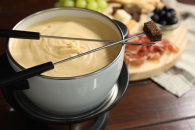 Fondue with tasty melted cheese, forks and piece of bread on wooden table