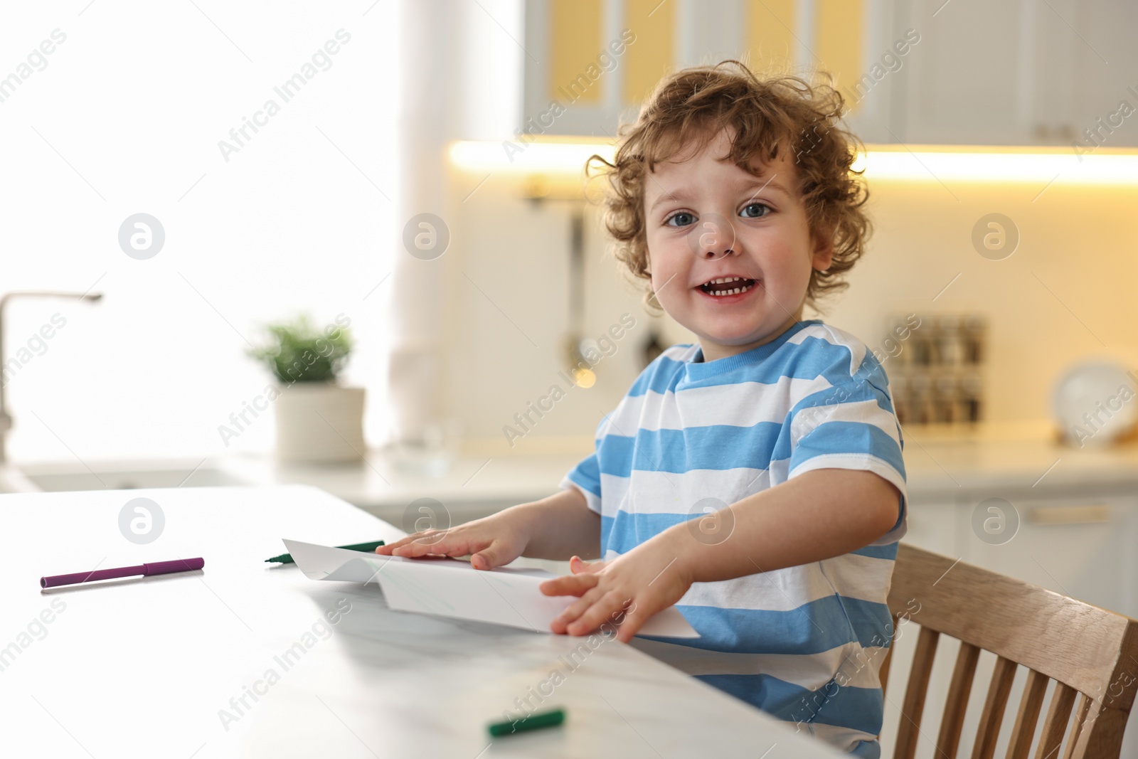 Photo of Cute little boy drawing with marker at table in kitchen. Space for text