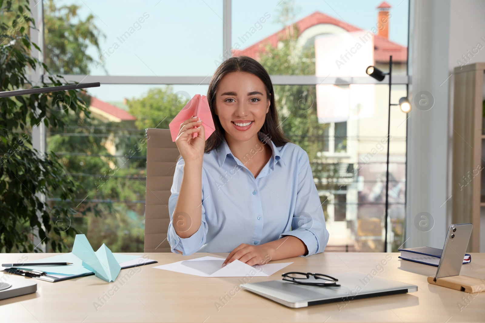 Photo of Beautiful young woman playing with paper plane at desk in office