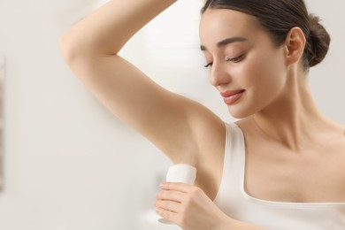 Beautiful young woman applying deodorant in bathroom