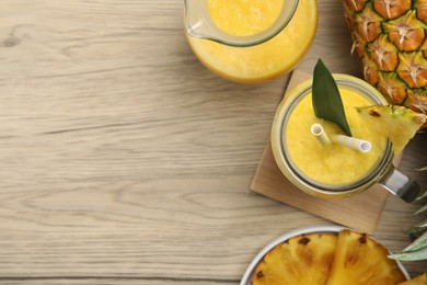 Tasty pineapple smoothie and fruit on wooden table, flat lay. Space for text
