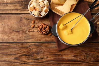 Photo of Pot of tasty cheese fondue, bread pieces and almonds on wooden table, flat lay. Space for text