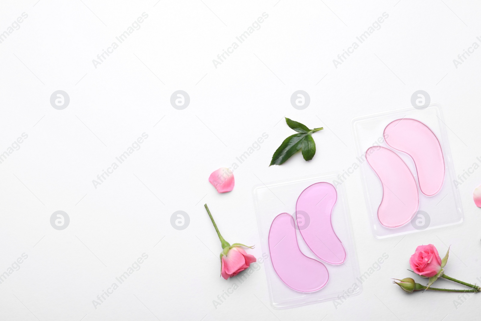 Photo of Packages with under eye patches and rose flowers on white background, flat lay. Space for text