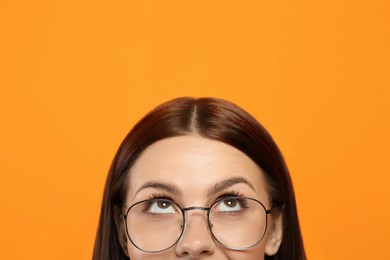 Photo of Woman in stylish eyeglasses looking up on orange background, closeup