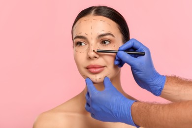 Doctor with pencil preparing patient for cosmetic surgery operation on pink background