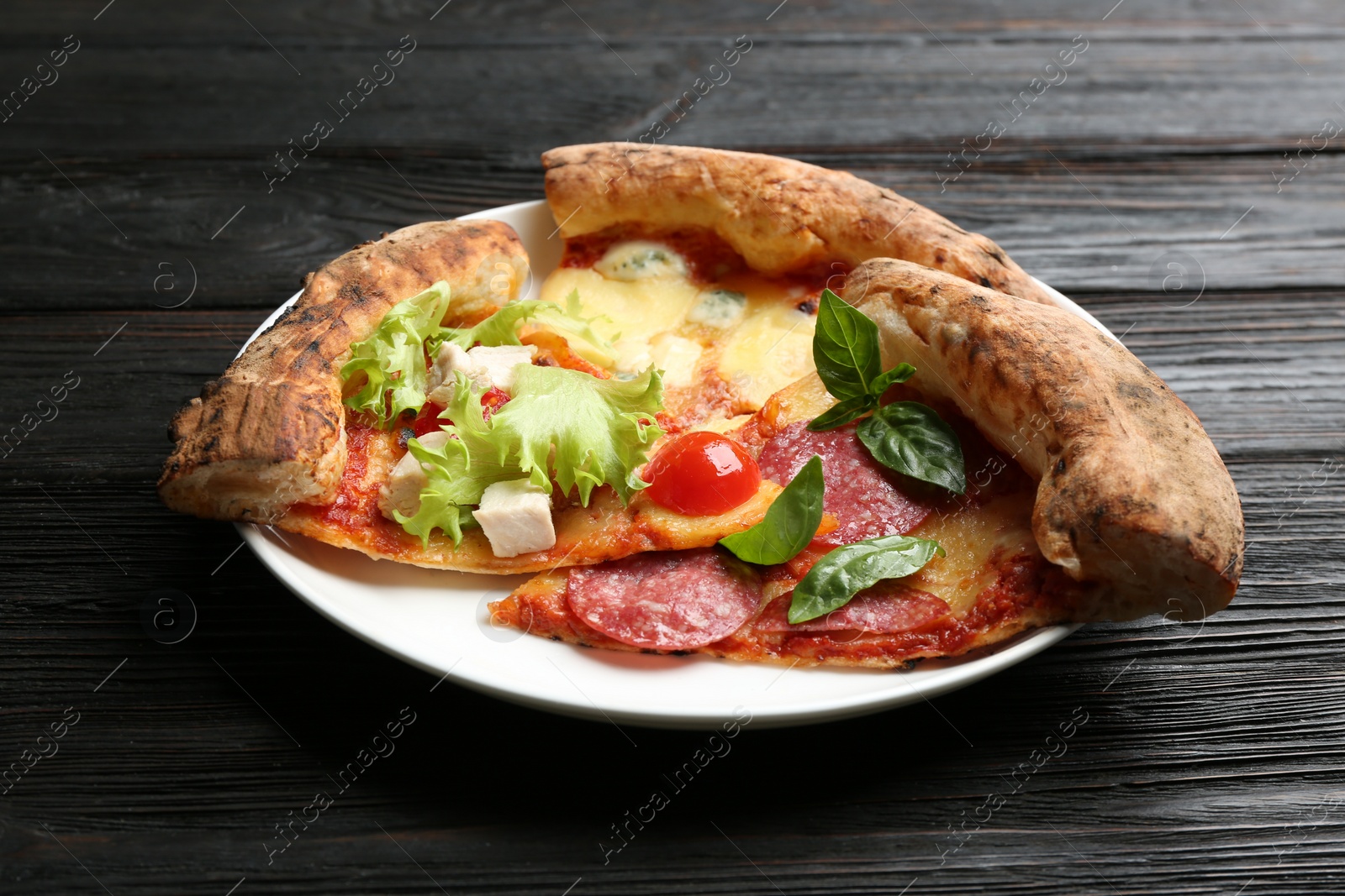 Photo of Slices of different delicious pizzas on black wooden table