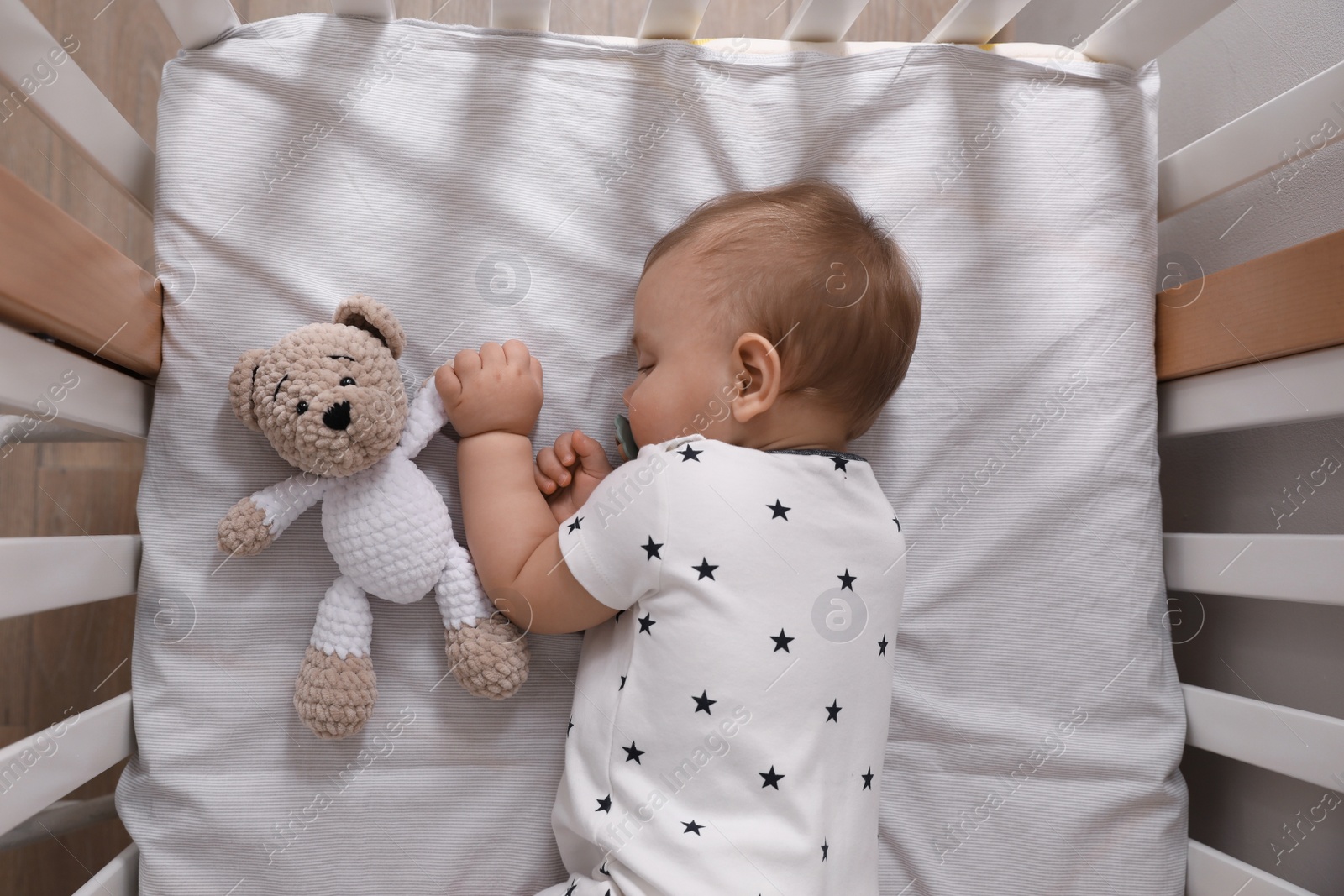 Photo of Adorable little baby with pacifier and toy sleeping in crib indoors, top view