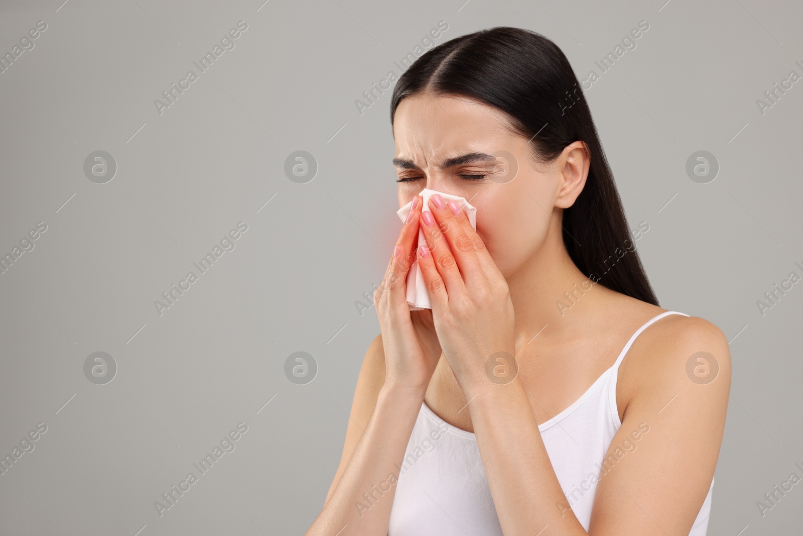 Photo of Suffering from allergy. Young woman blowing her nose in tissue on light grey background. Space for text