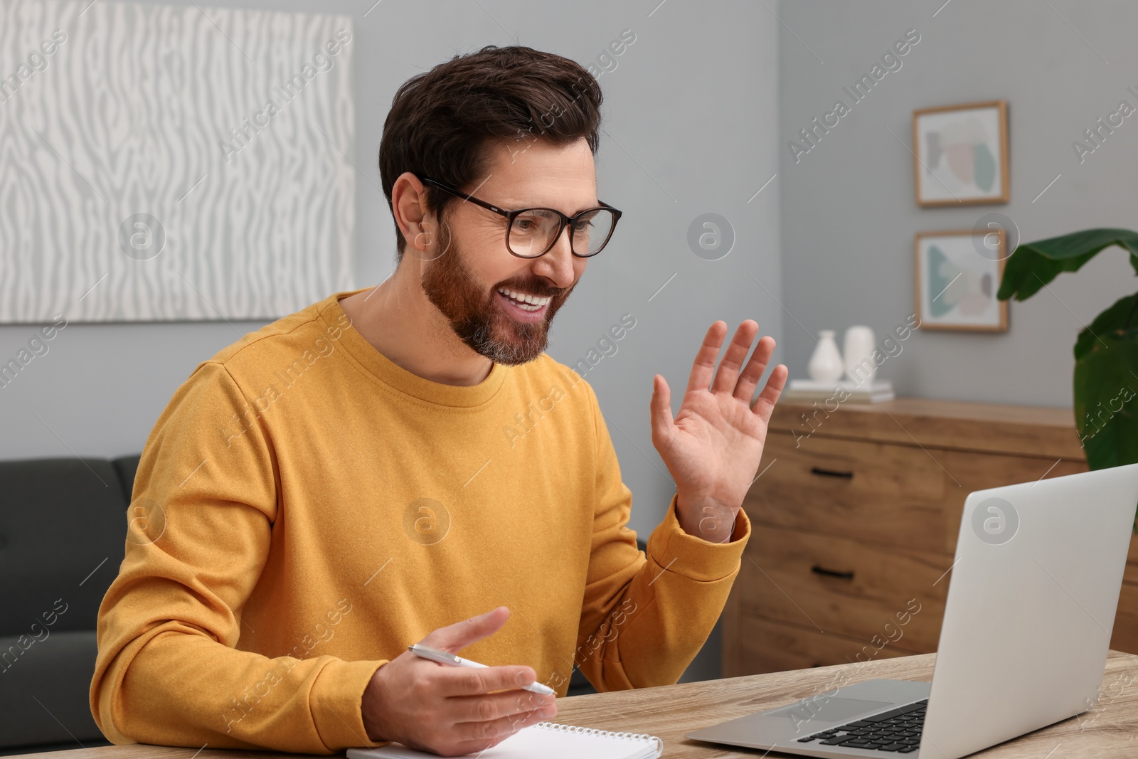 Photo of Man greeting someone during video chat via laptop at home